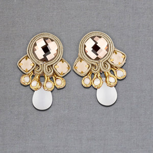 Hübsche kleine Soutache-Ohrringe mit goldfarbenen Bändern und schimmernden Steinen und Tropfe